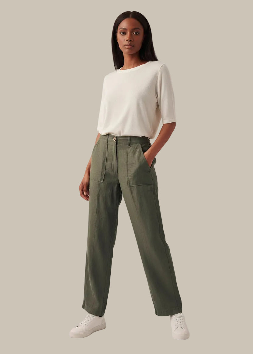 Woman wearing a white top and green pants on a plain background
