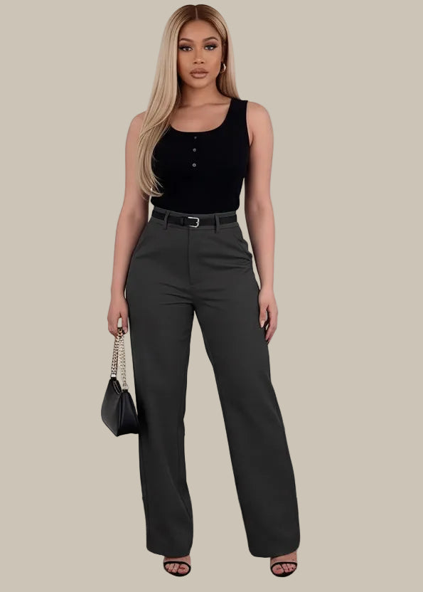 Woman wearing black high-waisted pants holding a black handbag on a wooden floor.