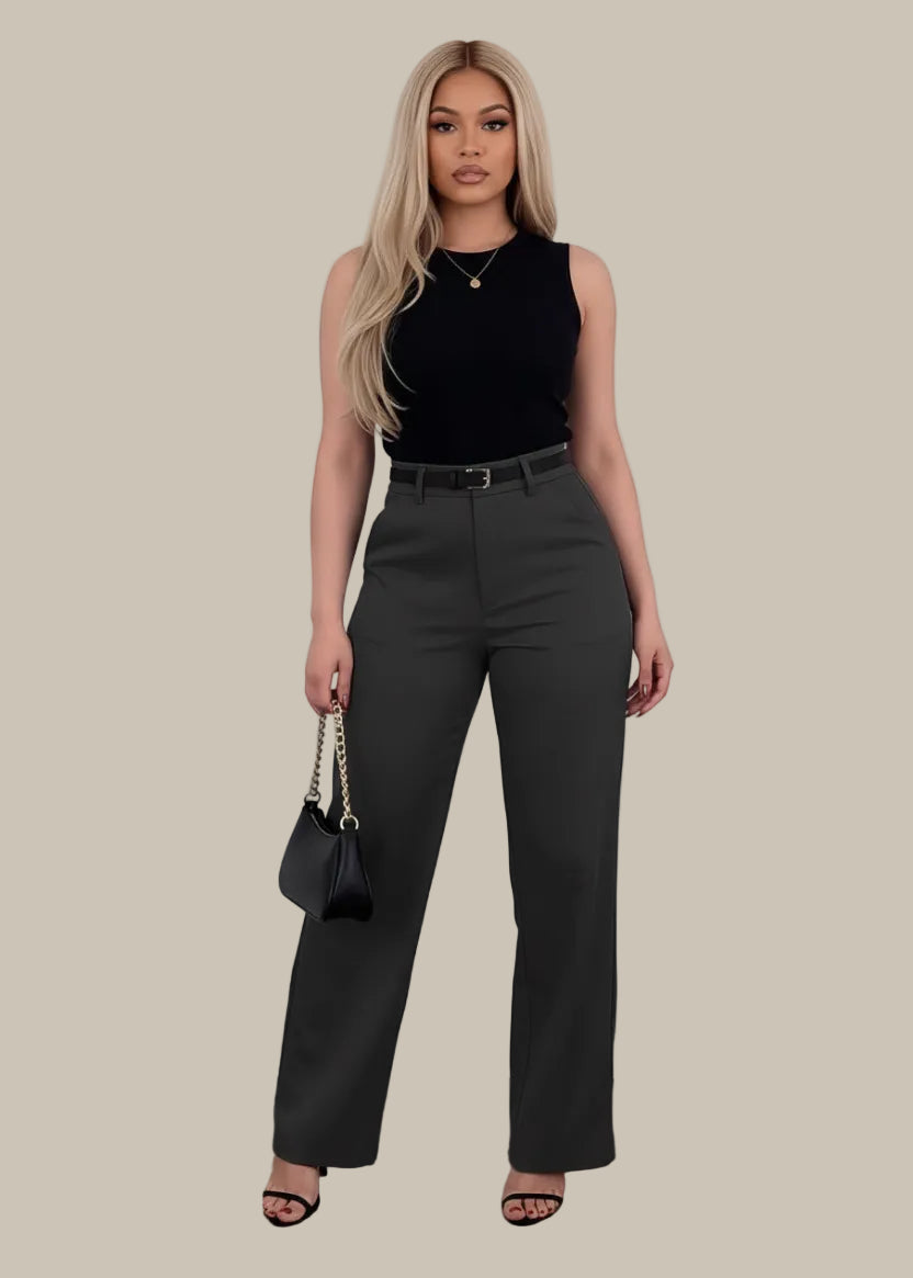 Woman wearing black high-waisted pants holding a black handbag on a wooden floor.