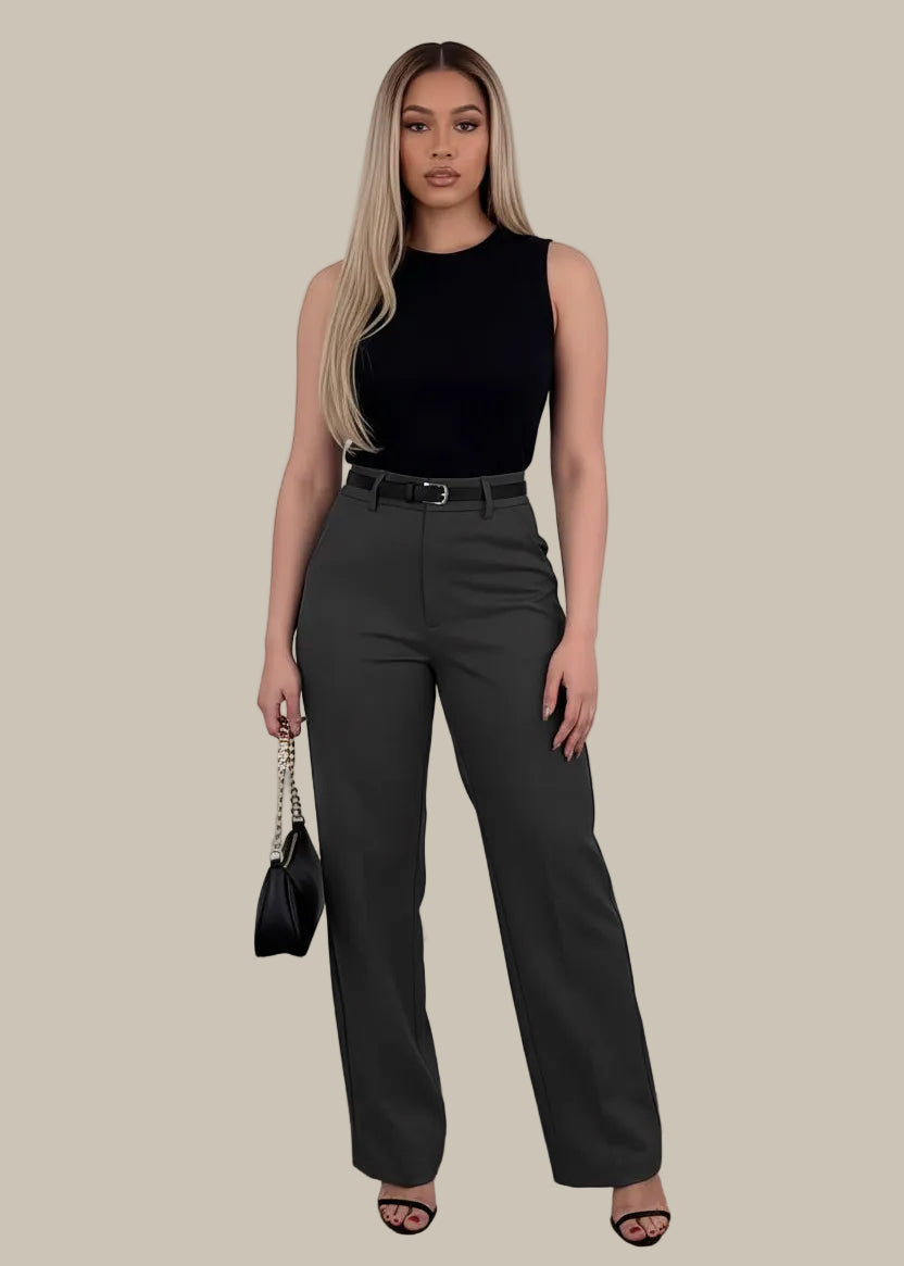 Woman wearing black high-waisted pants holding a black handbag on a wooden floor.