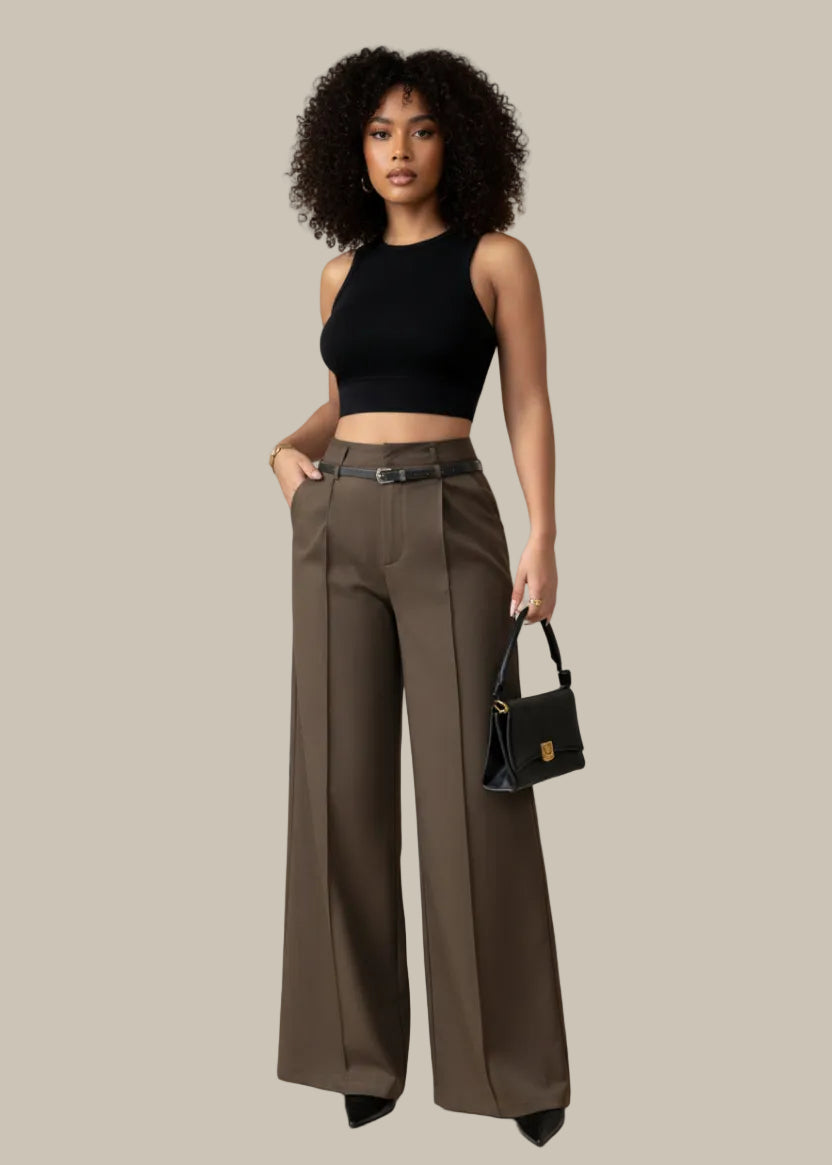 Person wearing brown wide-leg pants holding a black handbag against a neutral background