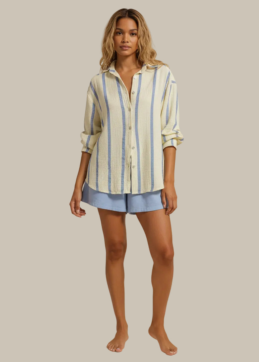 Woman wearing a striped shirt and blue shorts standing on a sunlit path.