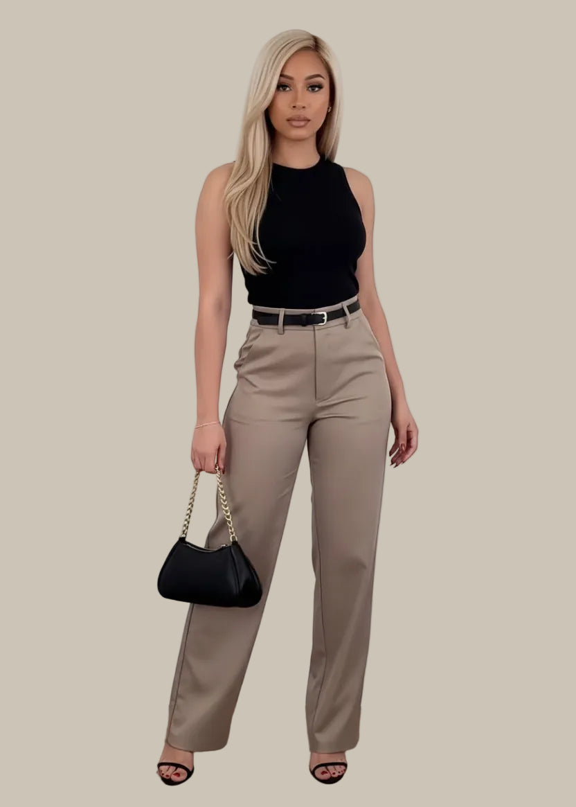 Woman wearing beige pants with a black top and sandals, holding a black handbag on a wooden floor.
