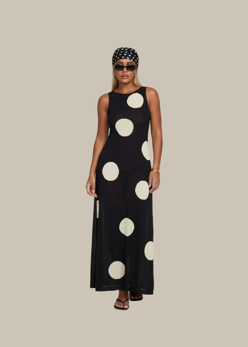 Woman in a polka dot dress standing in a stylish room with decor elements.