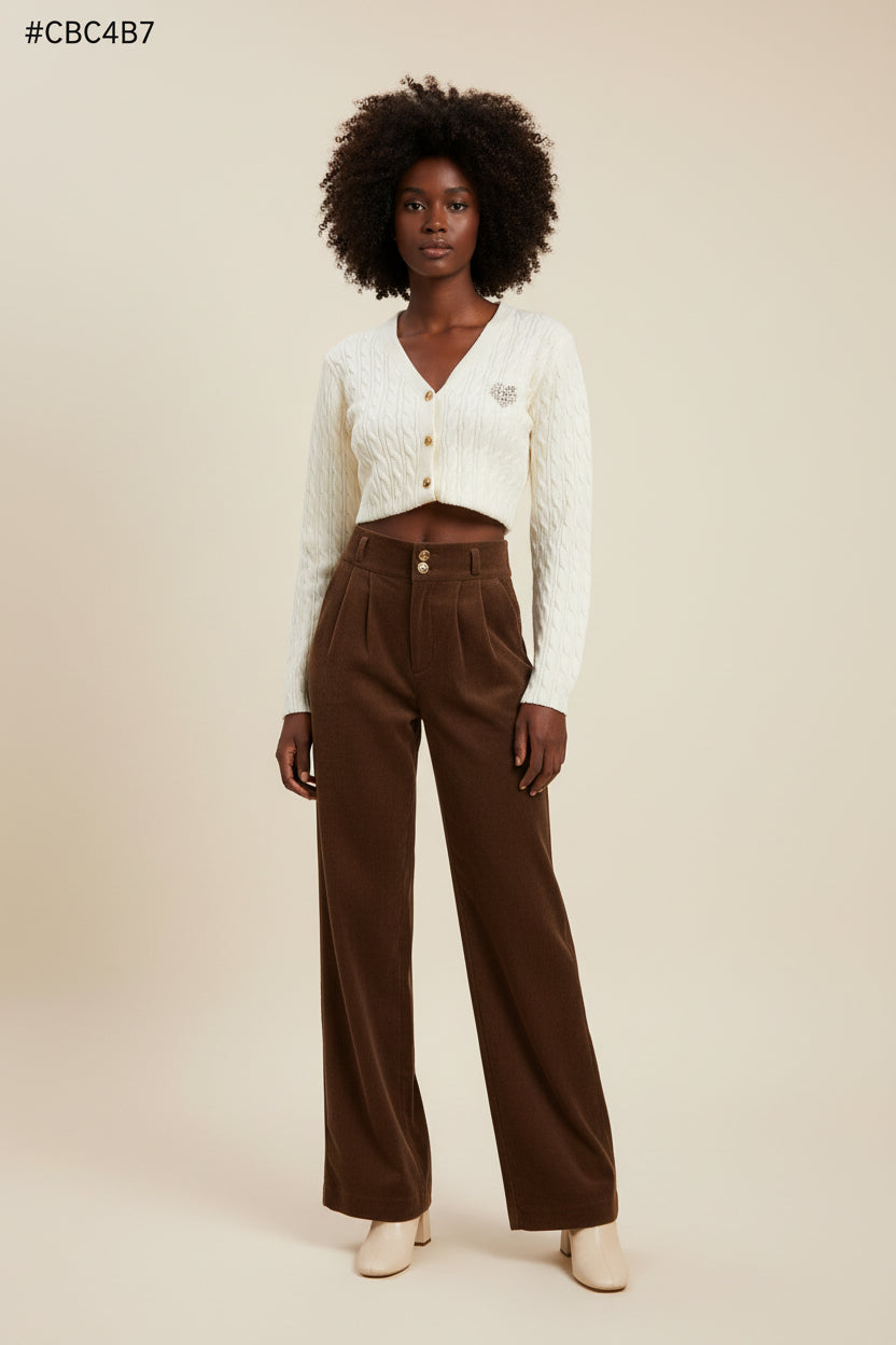 Person wearing a white cable knit cardigan and brown high-waisted pants sitting on a gray couch.