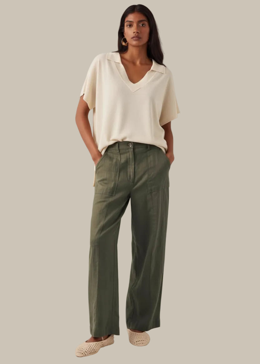 Woman wearing a white blouse and green pants against a neutral background