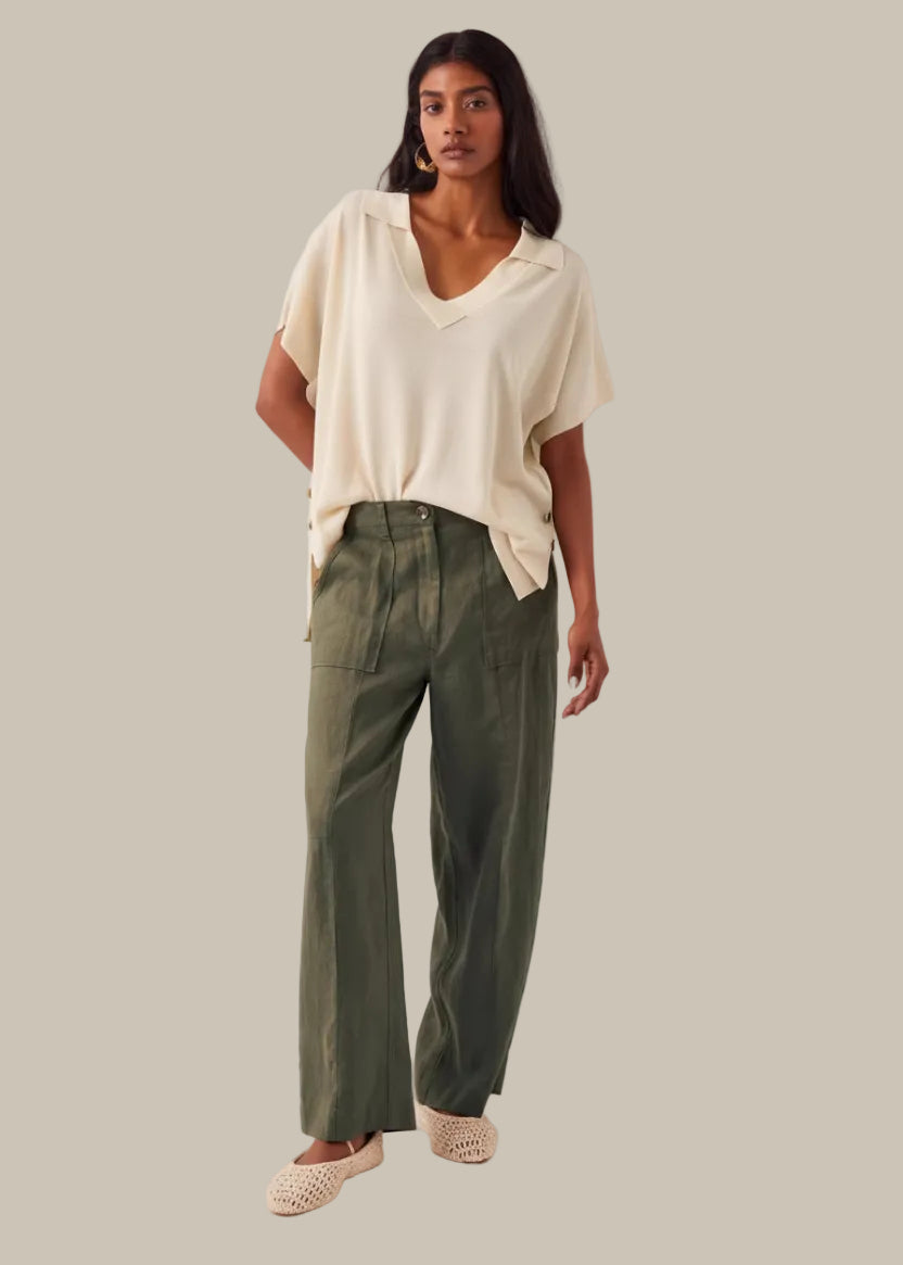 Woman wearing a cream top and green pants against a white background