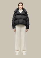 Person wearing a black puffer jacket and white pants on a beige background