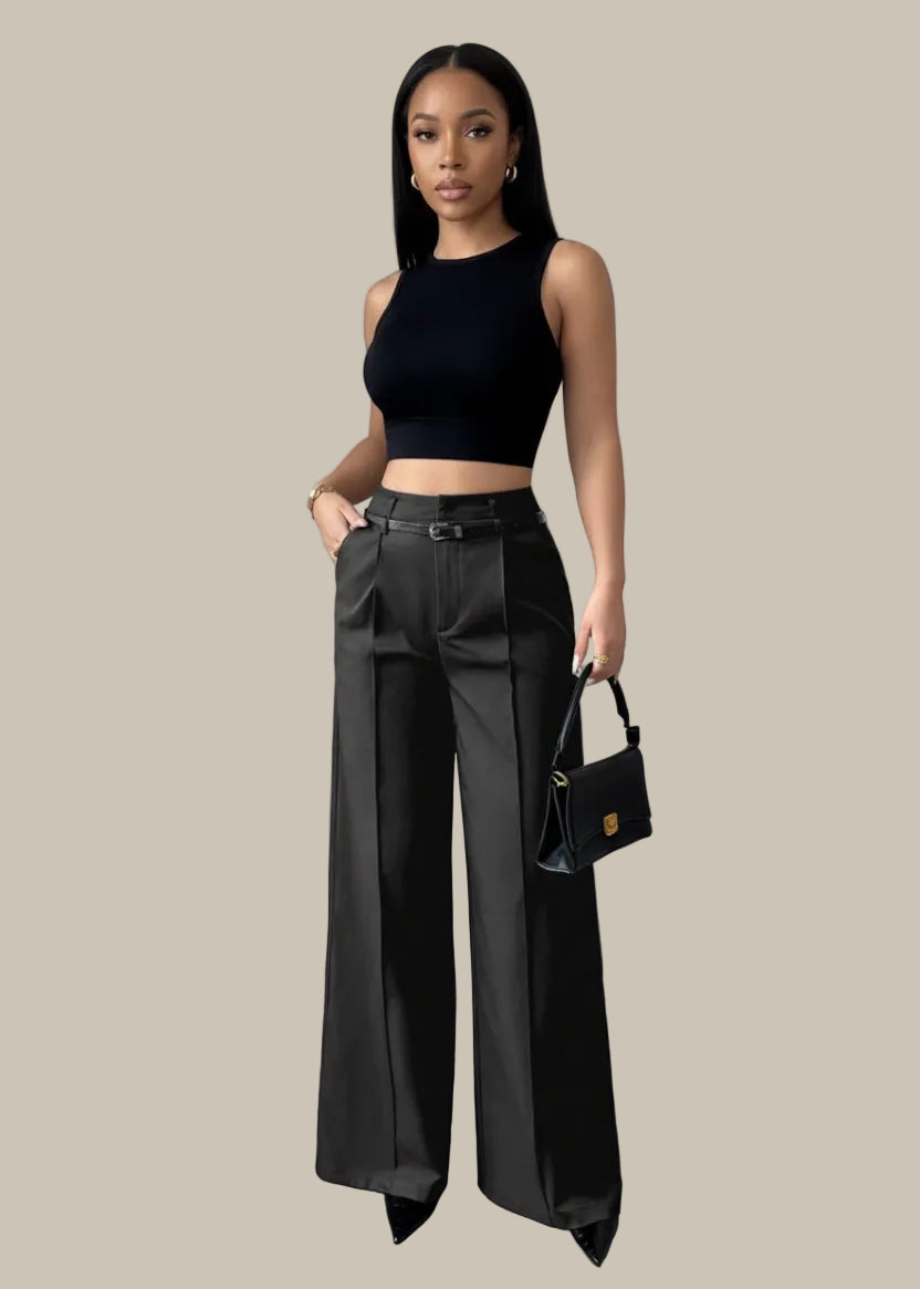 Person wearing black wide-leg pants holding a black handbag against a gray curtain background