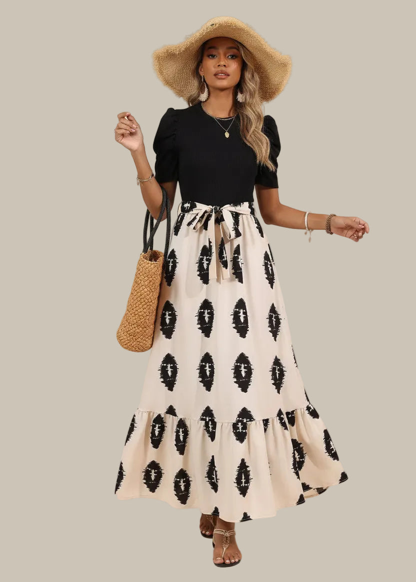 Woman wearing a black top and white patterned skirt with a straw hat and bag on a beige background