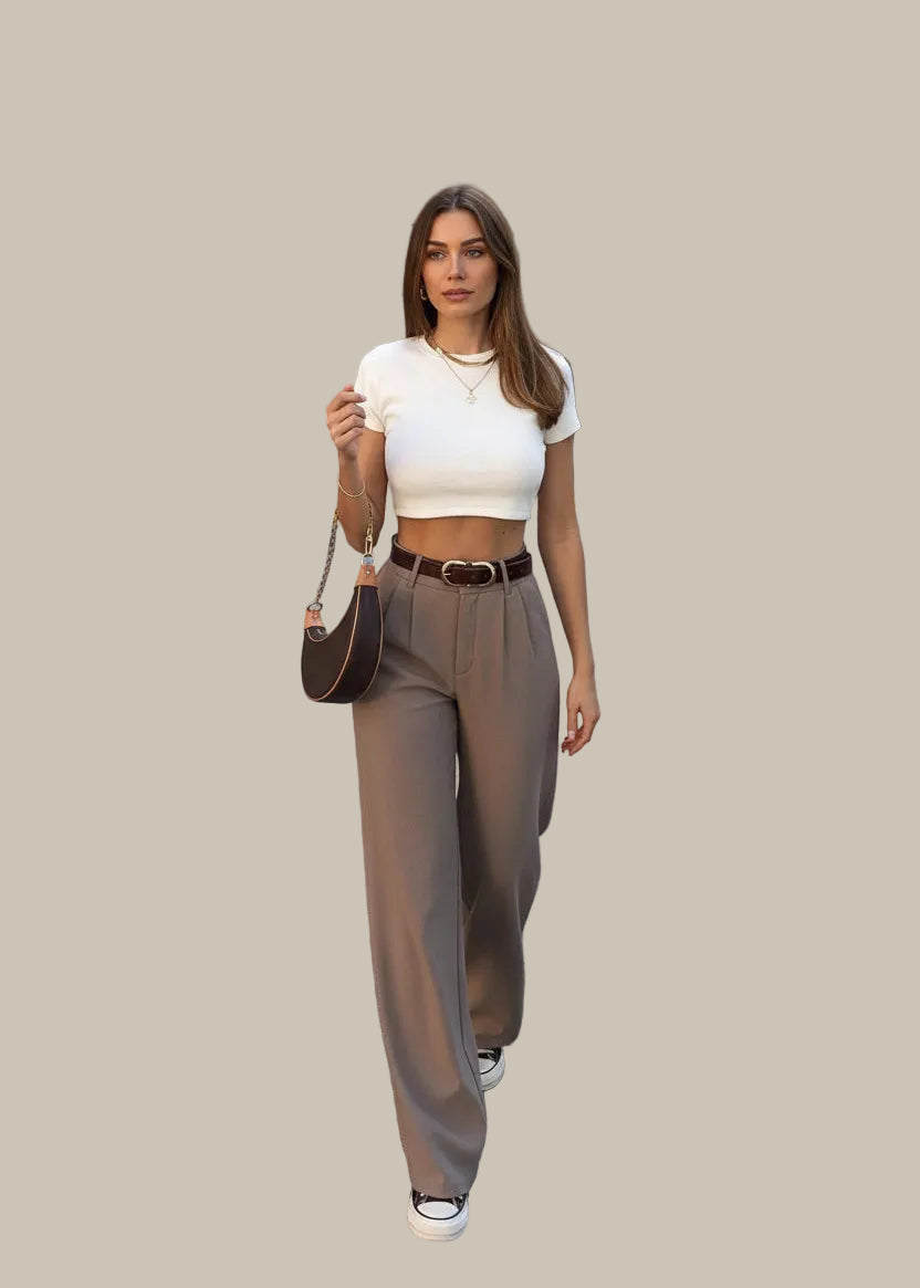 Woman walking on a street wearing a white crop top, beige high-waisted pants, and black sneakers.